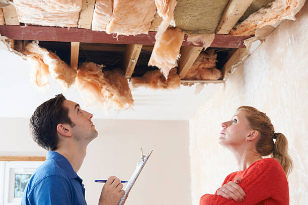 A man with a clipboard and a woman inspect a severely damaged ceiling with exposed insulation.