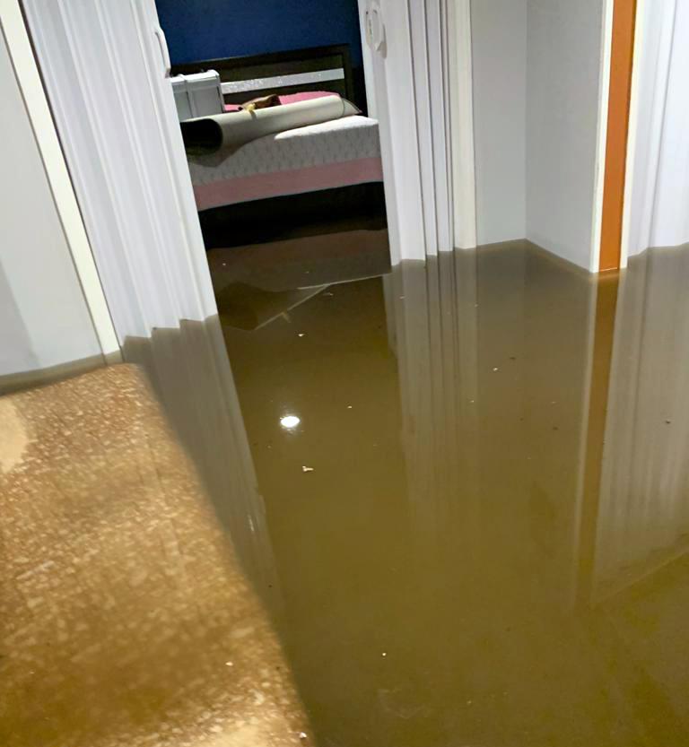 Murky brown floodwaters cover the floors of a house, extending into a visible bedroom.