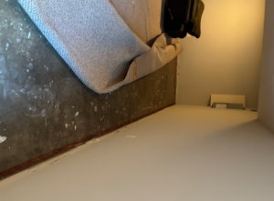 Rolled-back carpet reveals a paint-splattered concrete floor and light walls in a room