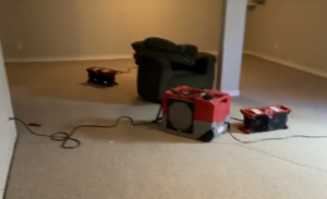 Three industrial air movers and an armchair are placed on light carpet in a spacious, empty room. affordable water damage repair services