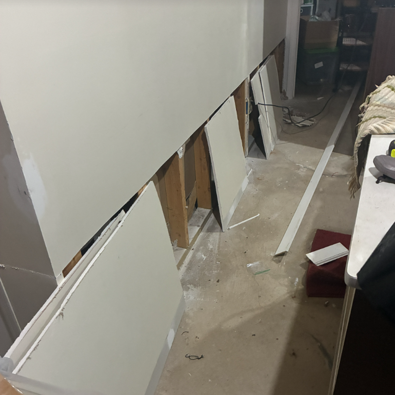 Basement wall with bottom drywall removed, exposing wooden studs and concrete floor for repair. TITLE
