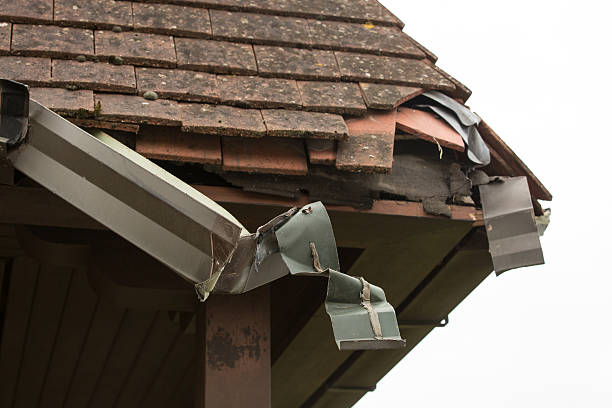 A severely damaged roof with broken tiles and a collapsed, bent gutter system. TITLE: