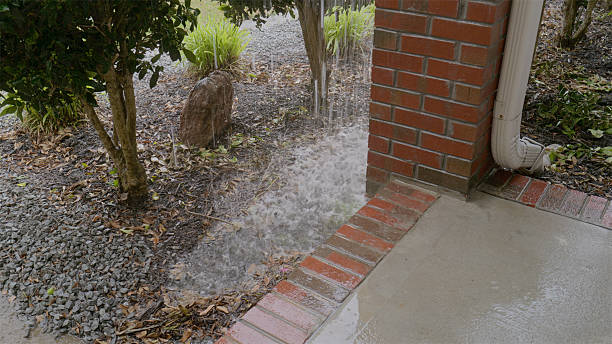 storm damage repair in Peoria Heavy rain pours from a downspout onto a concrete patio and gravel landscaping next to a