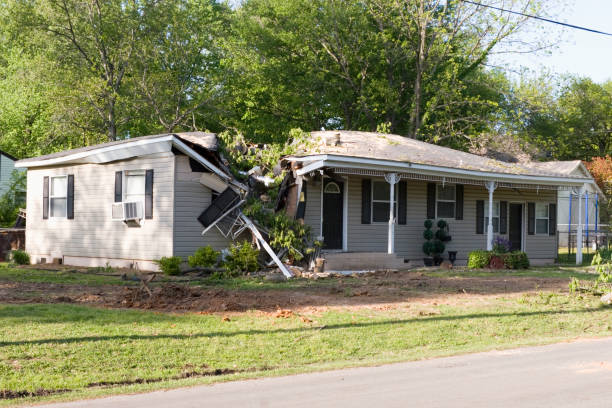 A residential house shows severe storm damage with a collapsed roof and debris on its left side