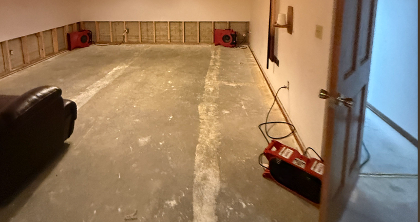 A room undergoing water damage restoration with exposed wall studs, concrete floor, and multiple