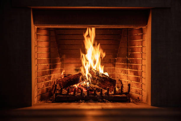 Fireplace burning firewood. Fire flames on wood logs, fireside bricks background. Cozy warm home at Christmas, dark room. Winter holidays greeting card fireplace safety
