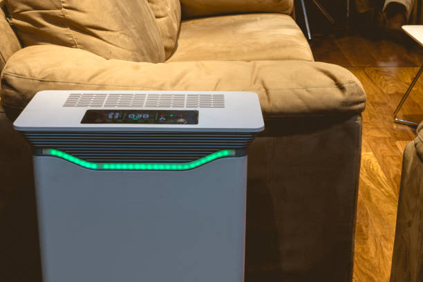 An air purifier with HEPA filter and UV lamp placed by the side of a sofa chair in the living room.