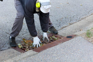 A Portrait Of A Black Man Picking Up Leaves On A Sewer Drain for Water Extraction in Aventura