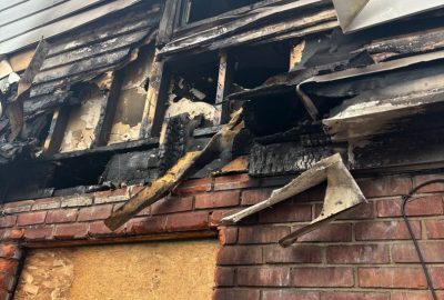 Residential fire mitigation is shown in a heavily destroyed garage structure with collapsed walls, exposed framing, and extensive fire-related debris scattered across the ground. The interior is charred and filled with burned materials, highlighting severe structural loss and smoke damage throughout the building.