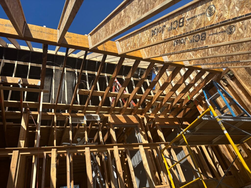 Extensive house framing and structural reconstruction and repairs due to fire damage, showing new wooden roof trusses, engineered I-joists, and scaffolding under a clear blue sky.