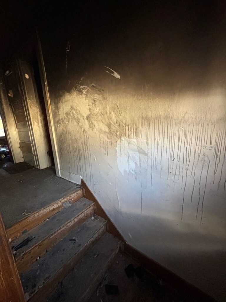 Close-up view of a wall damaged by heavy smoke and fire with black soot and water drip stains next to a staircase.