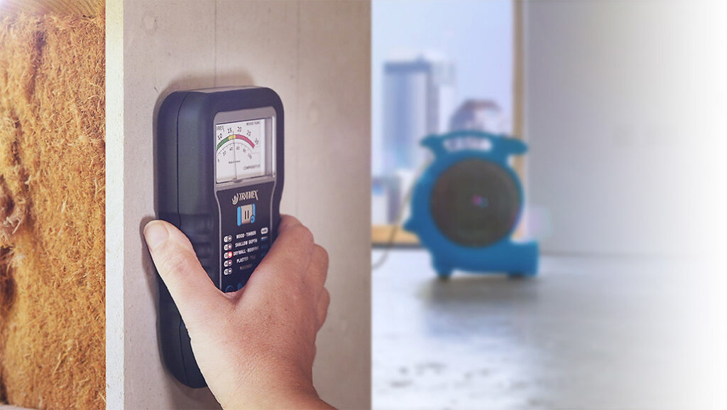 Restoration specialist using a digital moisture meter and a tablet to map out hidden water damage inside a drywall during the clean up process
