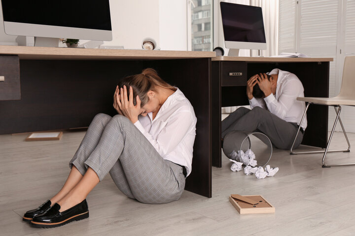Employees follow earthquake safety information by dropping, covering, and holding onto their desks.