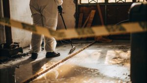 PC San c fire damage cleanup technician wearing protective gear while cleaning a damaged room with caution tape visible