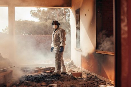 Worker in protective gear inspecting smoke-damaged interior after a fire