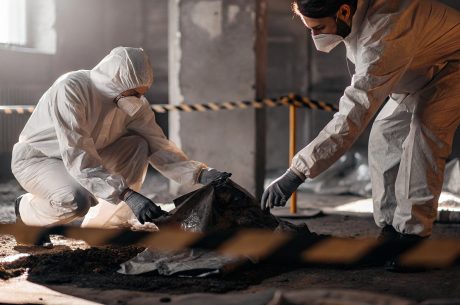 Technicians wearing protective suits handling biohazard waste disposal after cleanup in a contaminated area