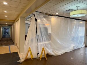 A hotel hallway leads to an area under renovation, sealed off by clear plastic sheeting and caution