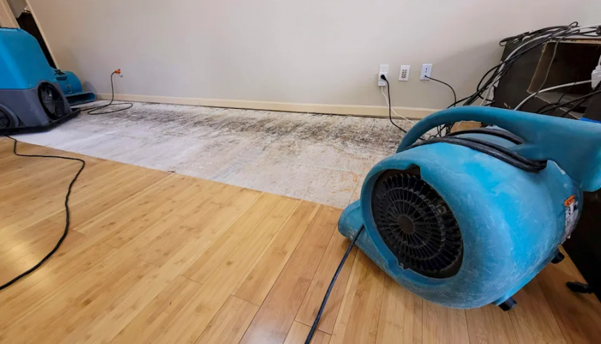 technician setting up industrial drying fans and dehumidifiers in a flooded living room