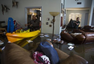 Homeowner assessing a flooded living room with standing water and damaged furniture
