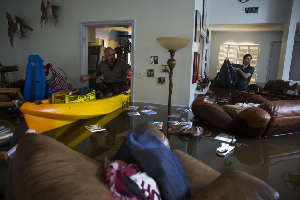 Homeowner assessing a flooded living room with standing water and damaged furniture
