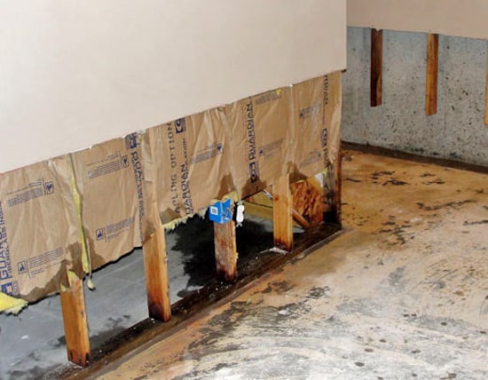 Technician examining water-weakened framing behind removed drywall