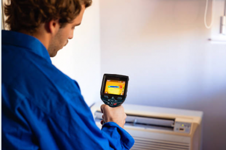 A certified restoration technician in a blue PuroClean uniform conducting a moisture assessment inside a water-damaged Ambler PA home; holding a thermal imaging camera with visible moisture readings on-screen| Insurance Claim Restoration in Ambler
