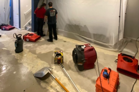 Aerial or wide-angle photo of a professional water damage restoration team in action inside a flooded home in a Pennsylvania suburb; workers in blue uniforms using extraction equipment on soaked floors | Insurance Claim Restoration in Abington