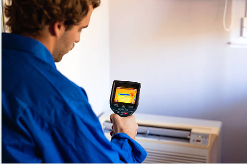 A certified restoration technician in a blue PuroClean uniform conducting a moisture assessment inside a water-damaged Ambler PA home; holding a thermal imaging camera with visible moisture readings on-screen| Insurance Claim Restoration in Ambler