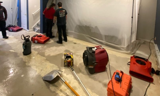 Aerial or wide-angle photo of a professional water damage restoration team in action inside a flooded home in a Pennsylvania suburb; workers in blue uniforms using extraction equipment on soaked floors | Insurance Claim Restoration in Abington