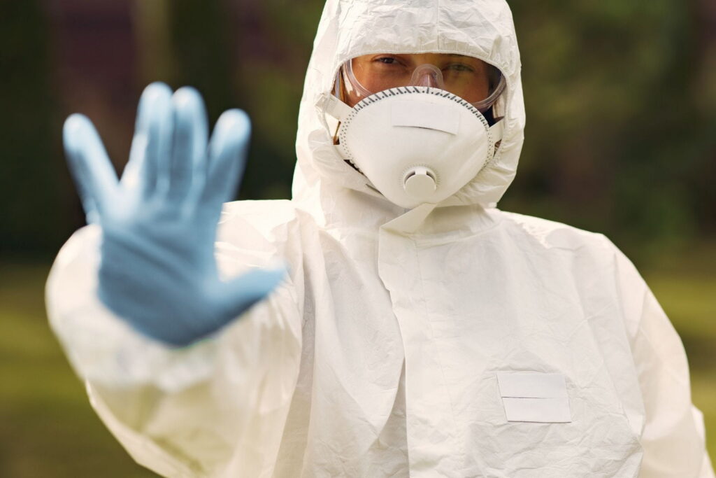 a home remediation specialist in a biohazard suit with his hand in the air