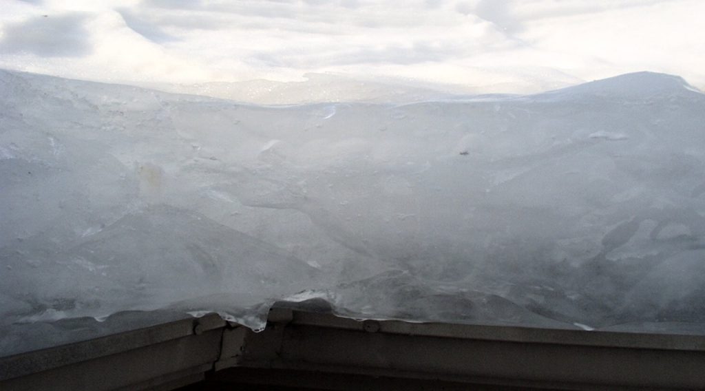 “Thick ice dam buildup along the roof edge, showing layered ice blocking proper drainage.”