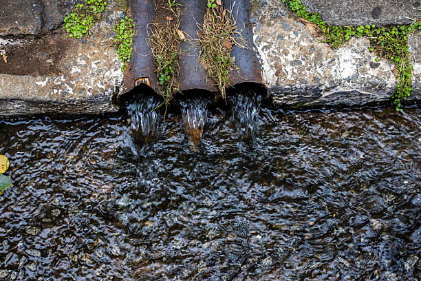 Three drainage pipes discharging water into a street gutter as part of the Sewage Backup in Queens