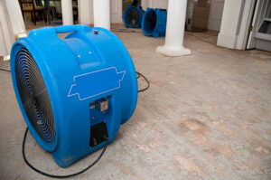 A large blue industrial drying fan sits on a stained concrete floor in a commercial space. Water Damage Restoration in Brooklyn