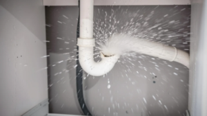 Water spraying from a burst white PVC P-trap pipe under