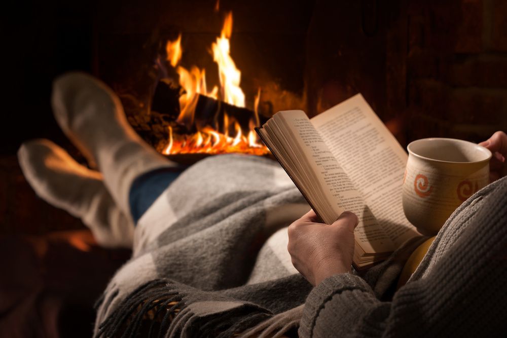 Woman reads book next to fire place. Winter fire safety tips.