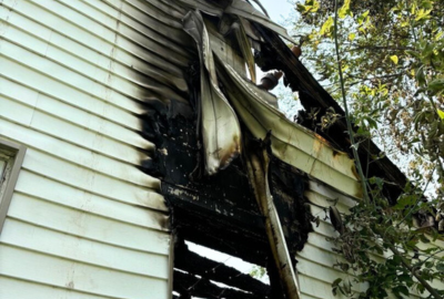 Photo of a home exterior with visible fire damage and melted siding, showing the importance of fire resilience during post-fire reconstruction.