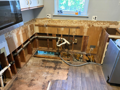 Kitchen under renovation with exposed plumbing, subfloor, and wall framing during water damage repair, showing the early stages of code-compliant reconstruction by PuroClean of Waterford Township