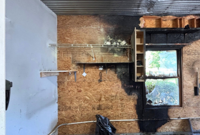 Charred wall and burned shelving inside a home after a fire, showing heavy soot damage near a window, requiring professional smoke damage restoration.