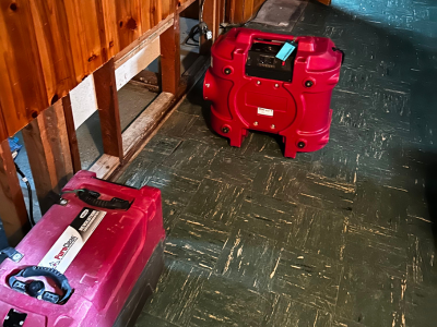 Biohazard cleanup and water damage restoration equipment, including air movers and dehumidifiers, in a residential space with exposed walls, being used to mitigate the effects of water damage and prevent further contamination by PuroClean of Waterford Township.