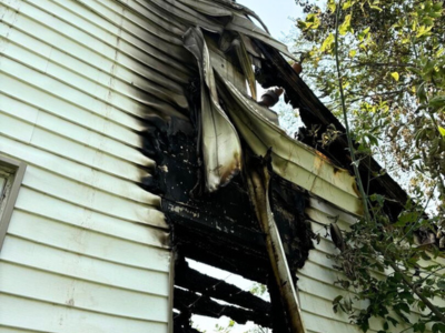 Photo of a home exterior with visible fire damage and melted siding, showing the importance of fire resilience during post-fire reconstruction.