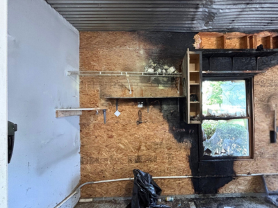 Charred wall and burned shelving inside a home after a fire, showing heavy soot damage near a window, requiring professional smoke damage restoration.