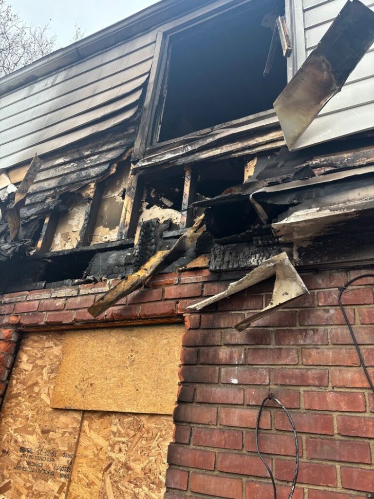 Residential fire mitigation is shown in a heavily destroyed garage structure with collapsed walls, exposed framing, and extensive fire-related debris scattered across the ground. The interior is charred and filled with burned materials, highlighting severe structural loss and smoke damage throughout the building.
