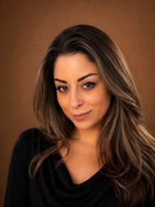 Portrait of a woman with long brown hair and a subtle smile against a warm brown background