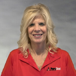 A smiling woman with blonde hair wearing a red shirt with the PureClean logo, against a gray background.