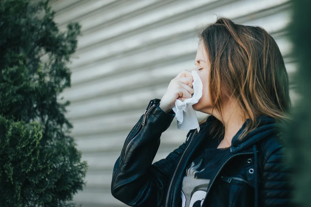 Woman blowing her nose with a tissue, likely suffering