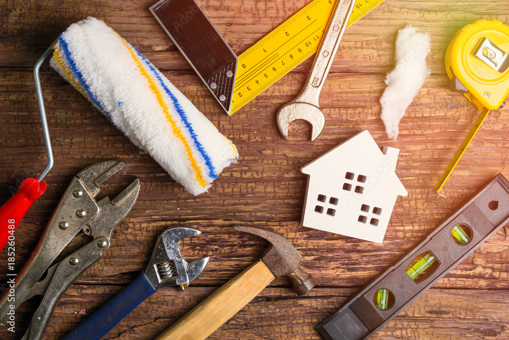 Various home improvement tools and a small house model are arranged on a rustic wooden surface