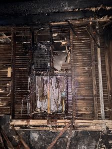 Residential fire mitigation is shown in a heavily destroyed garage structure with collapsed walls, exposed framing, and extensive fire-related debris scattered across the ground. The interior is charred and filled with burned materials, highlighting severe structural loss and smoke damage throughout the building.