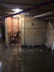 Flooded basement showing water accumulation on concrete floor with an office chair partially submerged, highlighting damage caused by minor leaks.