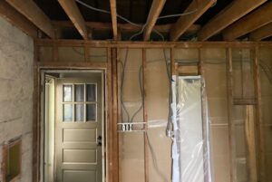 Home interior undergoing reconstruction and repairs due to fire damage, showing exposed wooden wall studs, ceiling joists, and new electrical wiring.