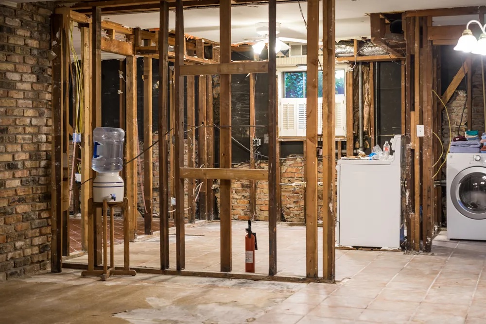 Interior room undergoing property damage restoration with exposed wood framing studs, a brick wall, and laundry appliances.